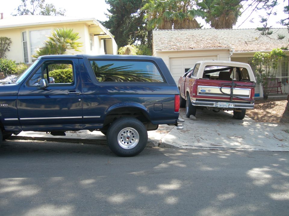 Side view of a 1994 Ford Bronco parked next to a red convertible SUV