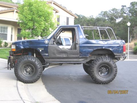 1994 Ford Bronco - This modified blue pickup truck features a custom roll cage and off-road tires, with its doors removed.