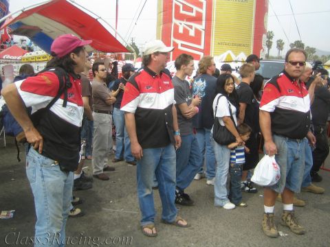 1990 Ford Bronco - group of men in matching red, white and black team shirts and jeans stand in a crowd near a yellow Tecate banner.