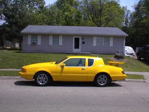 1986 Mercury Cougar - A bright yellow 1986 Mercury Cougar LS is parked on the street in front of a modest house.