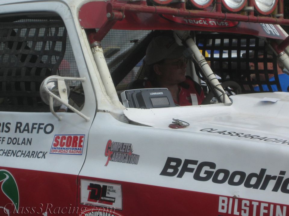 Driver seated in a white off-road race truck cab with BFGoodrich and Raffo lettering