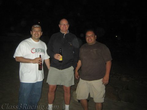 1990 Ford Bronco - Three men stand together outdoors at night holding drink bottles, smiling for the camera in low light.