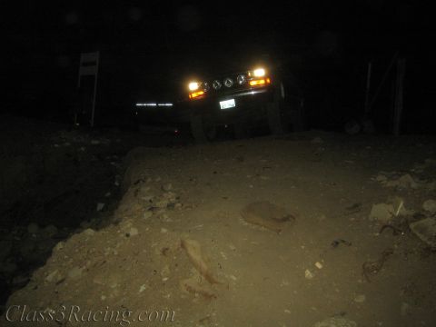 1990 Ford Bronco - vehicle with headlights and amber marker lights glowing sits behind a mound of dirt and rock in near-total darkness.