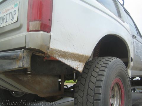 1990 Ford Bronco - Close-up of a rust-edged white pickup rear quarter and tail light with a California PICKUPITUP plate, loaded on a trailer.