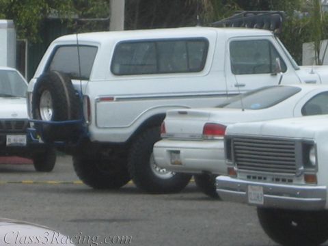 1990 Ford Bronco - white full-size Ford Bronco with a rear-mounted spare sits beside an older white Ford pickup in a parking lot.
