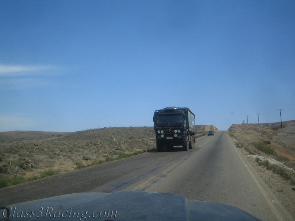 Dark off-road truck driving down a desert highway through scrubland