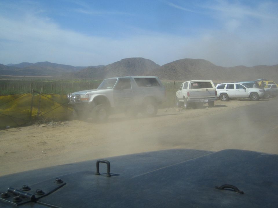 Silver lifted Bronco-style SUV and other trucks parked in a dusty desert lot