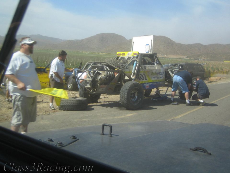 Crew works on a number 102 off-road race buggy stopped at roadside