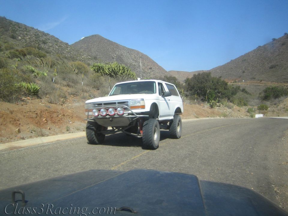 White lifted Bronco-style SUV with front light bar on a winding desert road