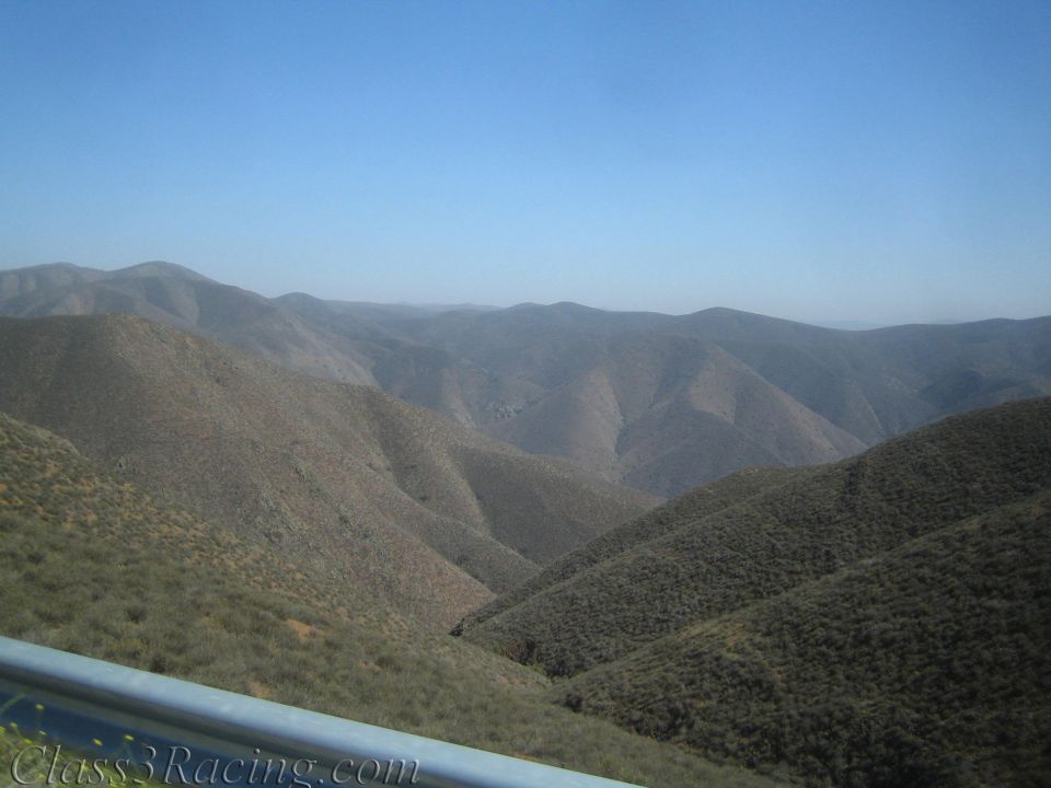Rolling dry brush-covered hills under a clear blue sky behind a guardrail
