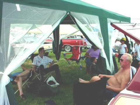 1992 Ford Mustang - Attendees relax under a canopy at an outdoor car show event, with vintage vehicles on display.