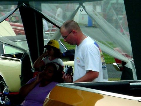 1992 Ford Mustang - A group of people are gathered under a tent, with a yellow and red car partially visible in the background.