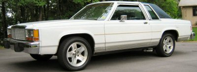 1985 Ford LTD Crown Victoria - White 1985 Ford Crown Victoria LTD coupe parked on asphalt with trees in background.