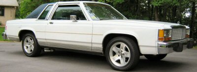 1985 Ford LTD Crown Victoria - This white Ford sedan has a distinct vinyl roof and chrome accents, parked outdoors.