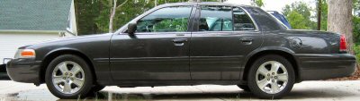 1985 Ford LTD Crown Victoria - Side profile of a dark gray sedan, likely a Ford Crown Victoria from the early 2000s.