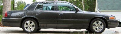 1985 Ford LTD Crown Victoria - Side profile of a dark gray sedan, likely a Ford Crown Victoria, parked outdoors.