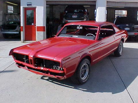 1967 Mercury Cougar - A red 1967 Mercury Cougar is parked in front of an open garage bay, with other vehicles visible inside.