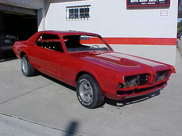 Red Mercury Cougar coupe shell in fresh paint outside a body shop, front three-quarter view