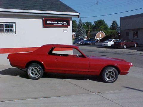 1967 Mercury Cougar - A red 1967 Mercury Cougar is seen parked outside an auto body shop, with other vehicles in the background.
