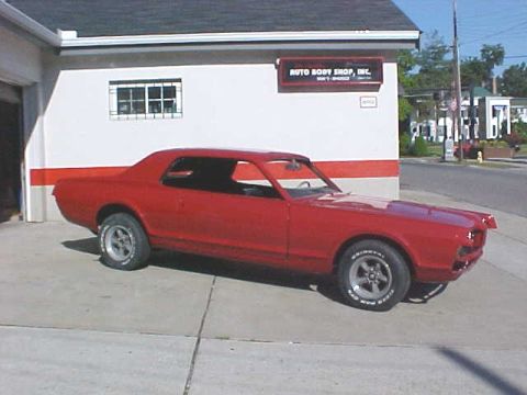 1967 Mercury Cougar - A red 1967 Mercury Cougar is parked in front of an auto body shop.