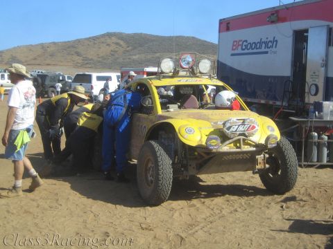 1990 Ford Bronco - crew services a yellow off-road race buggy in a desert pit next to a BFGoodrich Tires semi-trailer.