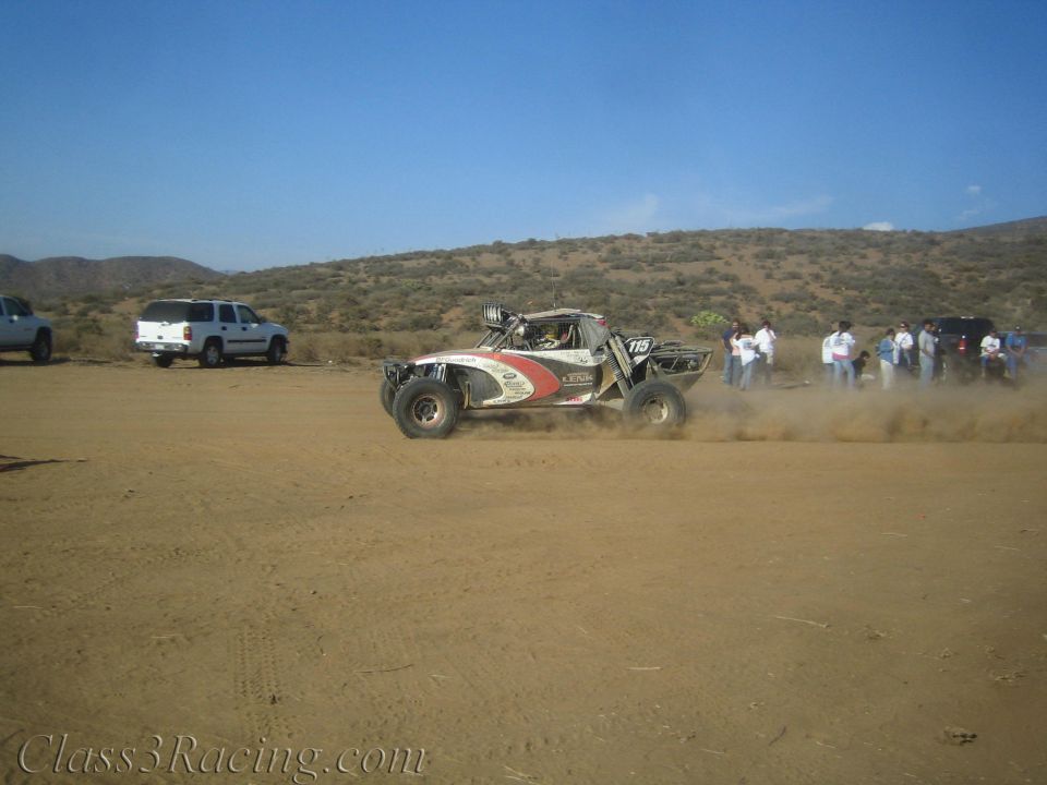 White and red off-road race buggy number 10 kicking up dust on a desert dirt course