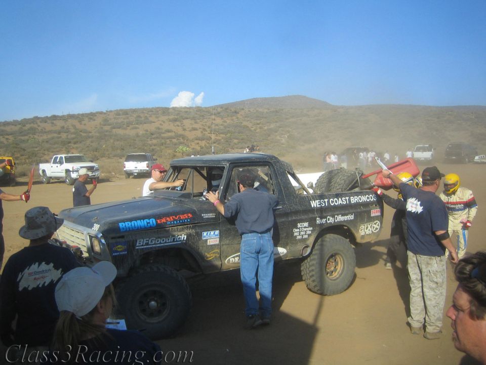 Black West Coast Broncos race truck number 300 refueled by crew in a desert pit