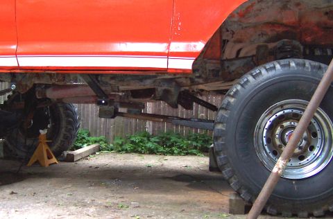 1978 Ford Bronco - The undercarriage of an orange vehicle is visible, with large tires and suspension components.