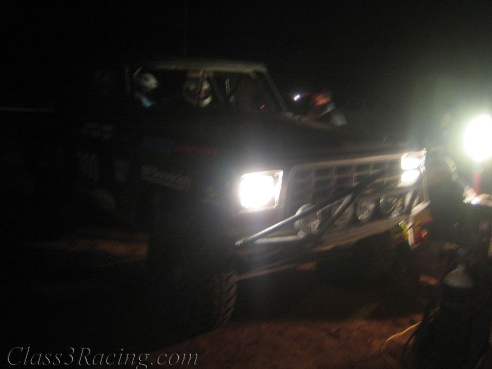 Off-road race truck with bright headlights at a dark night pit