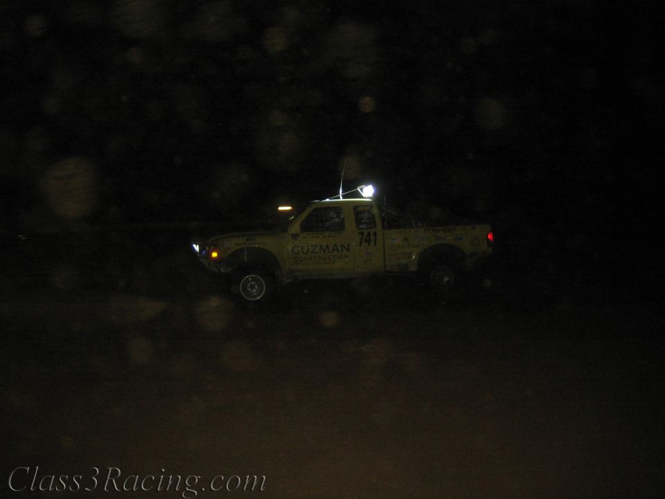 Yellow Guzman number 741 race truck on a dark course with lights on