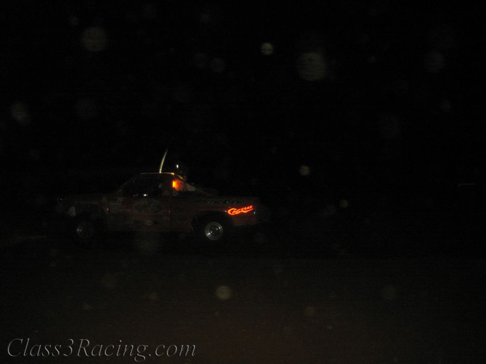 Faint off-road race truck with running lights on a dark night course