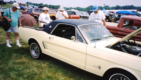 1979 Ford Ranchero - A cream 1965 Ford Mustang coupe is displayed with its hood open, surrounded by onlookers at an outdoor event.