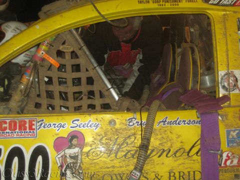 1990 Ford Bronco - driver works inside the cage of a yellow off-road race car lettered George Seeley and Bruce Anderson with a Magnolia florist livery.