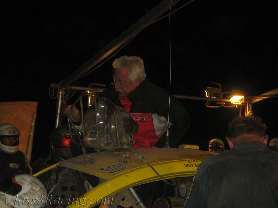 Gray-haired man working over the back of a yellow off-road race car at night