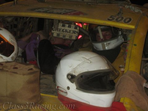 1990 Ford Bronco - driver in a white full-face helmet sits in the caged cockpit of a yellow off-road race car marked 500 at night.