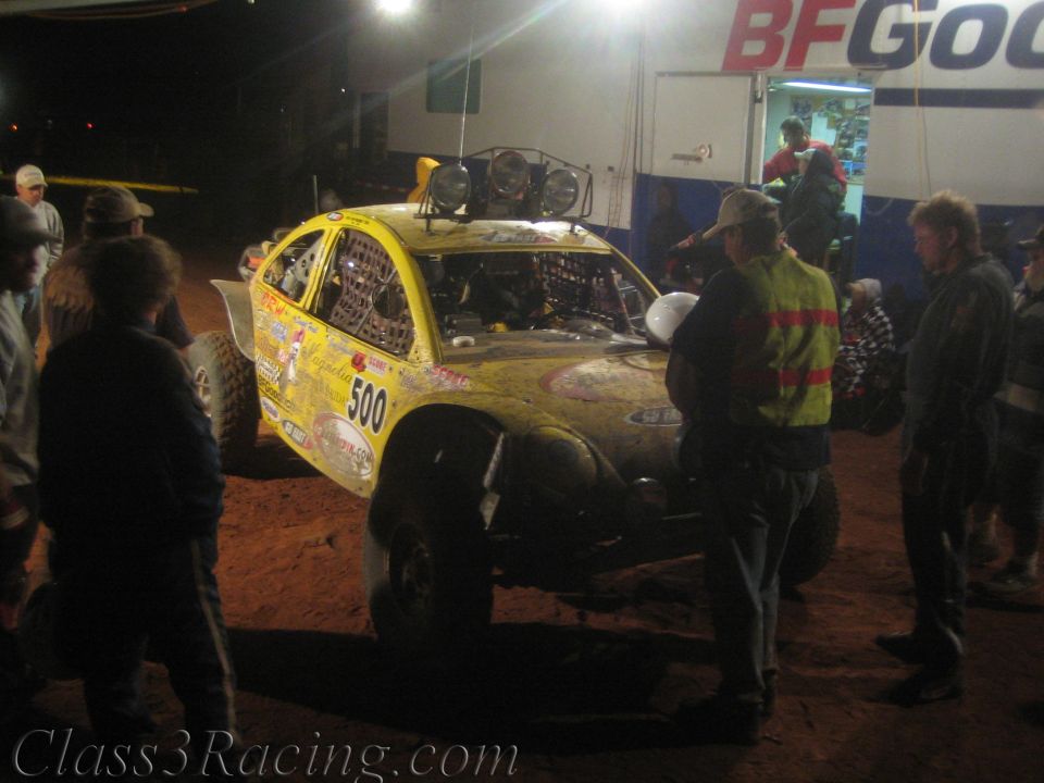 Yellow off-road race car number 500 surrounded by crew at a night pit