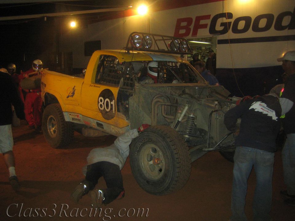 Yellow off-road race truck number 801 being worked on by crew at night
