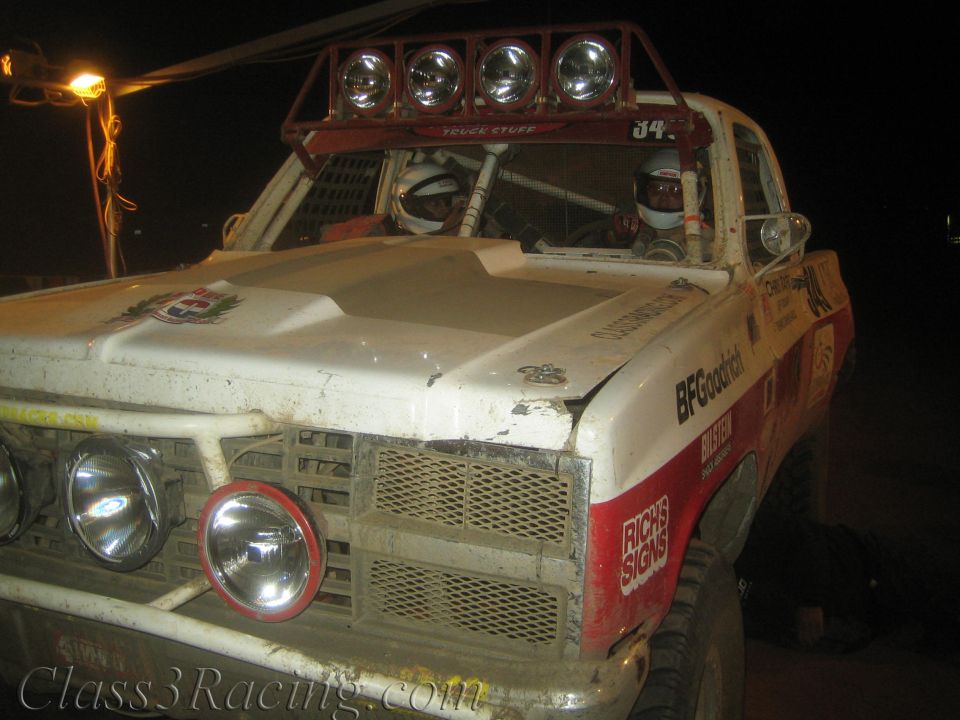 White and red off-road race truck with roof light bar at night