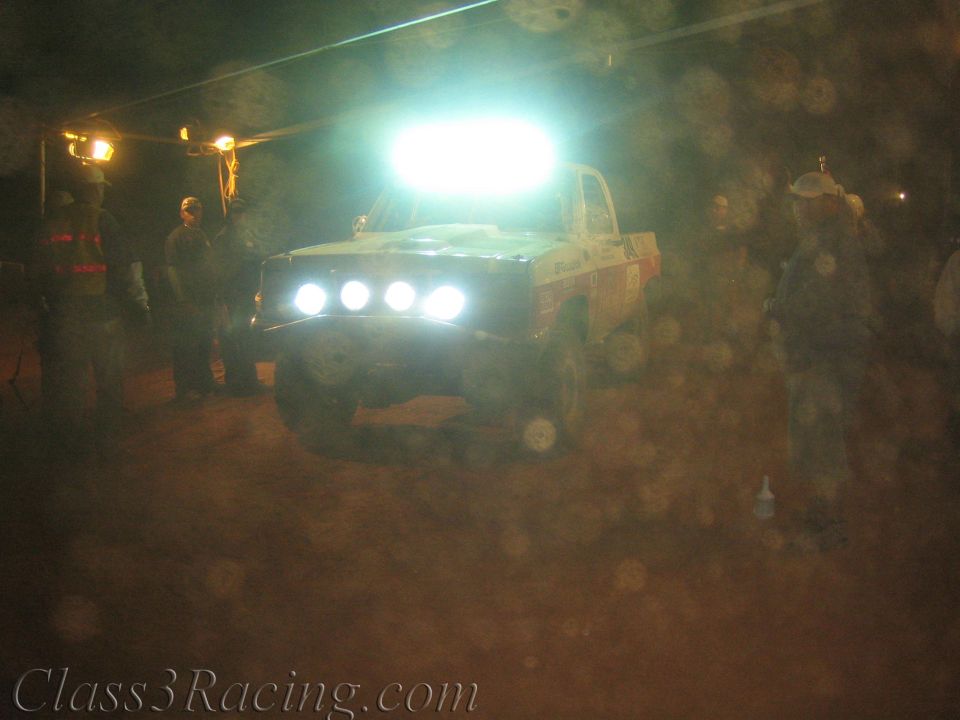Off-road race truck with glowing roof lights in a dusty night pit