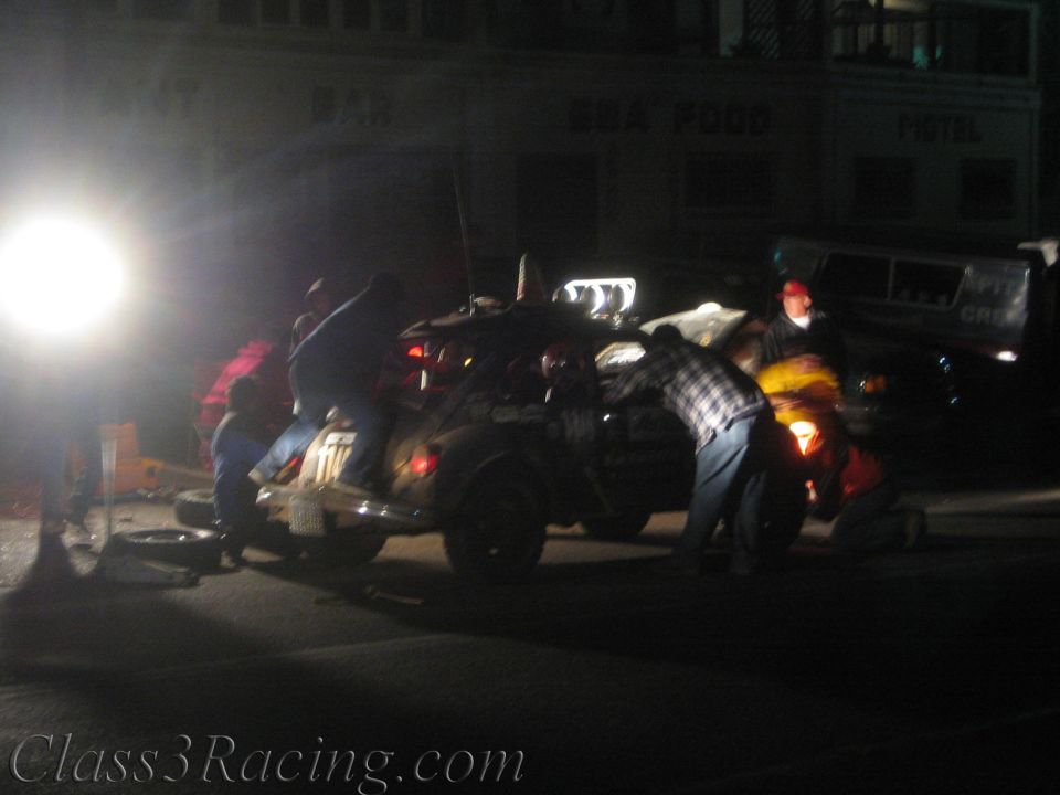 Crew working on a race car in a dark street in front of a motel at night