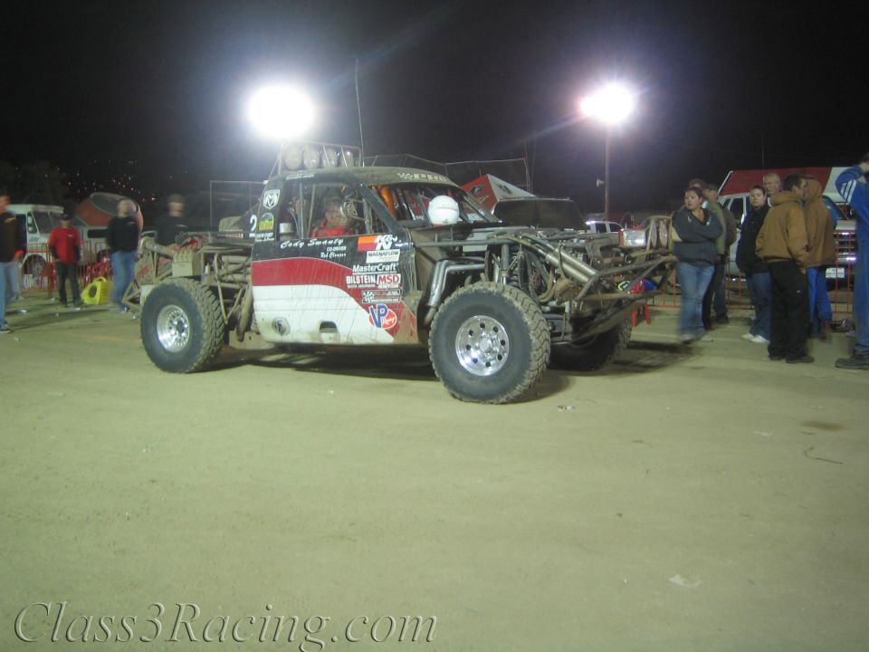 White and red open-chassis off-road race car number 2 in a lit dirt pit
