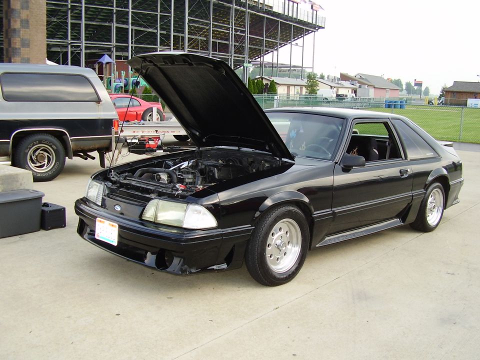 Black 1987 Ford Mustang with hood open, parked next to a black and grey SUV