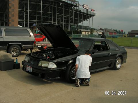 1988 Ford Mustang - A person works on a black coupe while a silver SUV is parked nearby at a track.