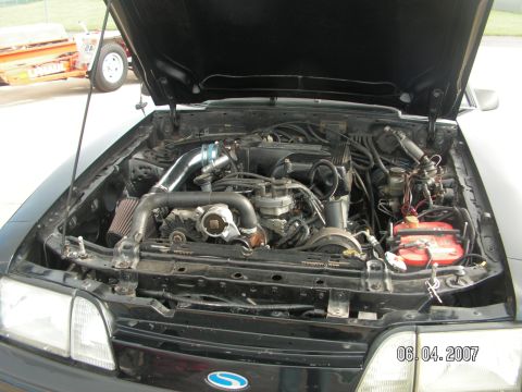 1988 Ford Mustang - The engine bay of a 1988 Ford Mustang is shown with the hood open, revealing the V8 engine and associated components.