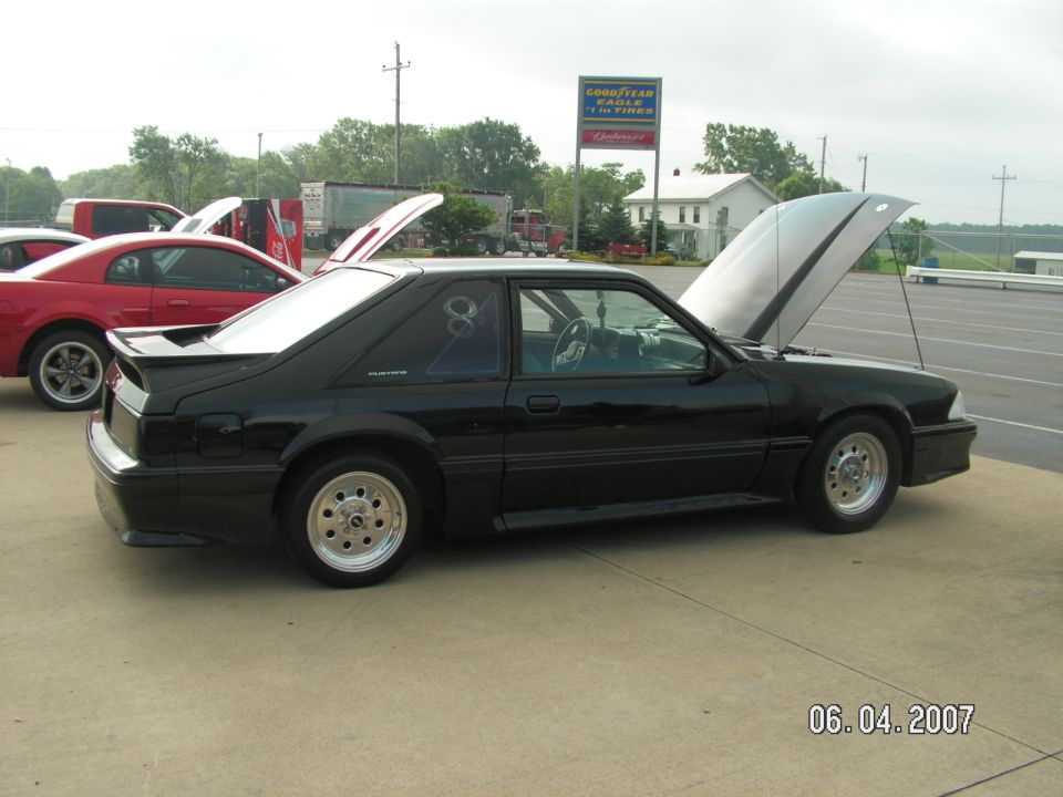 Black coupe with hood open, side view, aftermarket wheels, spoiler, and a graphic on the rear window