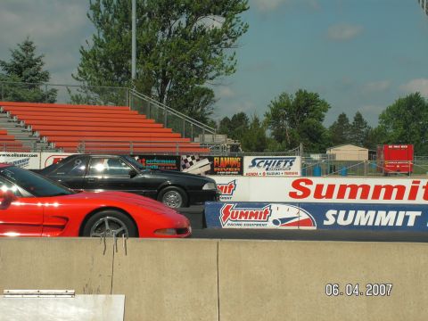 1988 Ford Mustang - Two cars are lined up at a drag strip, with grandstands and sponsor banners visible.