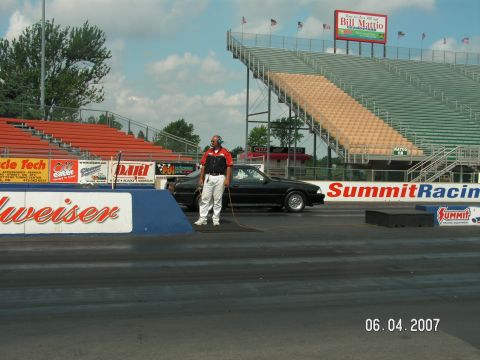 1988 Ford Mustang - A black 1988 Ford Mustang is parked on the drag strip with a man standing next to it.