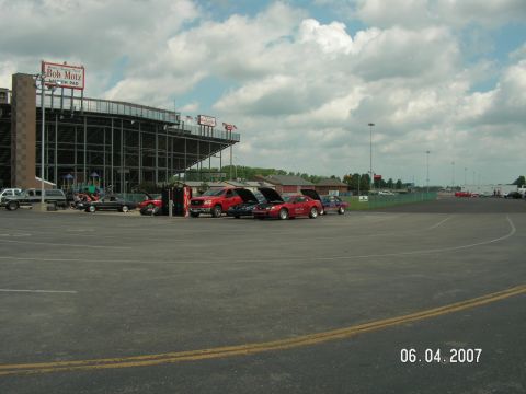 1988 Ford Mustang - Several cars are parked at a racetrack, with one red 1988 Ford Mustang prominently displayed.
