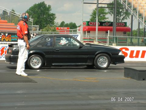 1988 Ford Mustang - A black 1988 Ford Mustang is staged on a drag strip with an official watching.