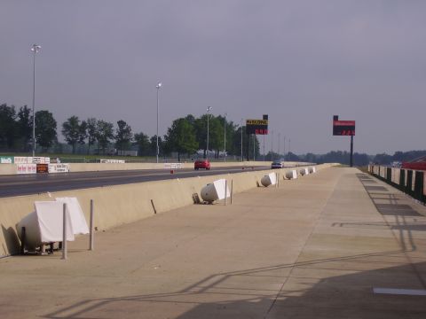 1988 Ford Mustang - A drag strip scene with two cars visible on the track under a cloudy sky.